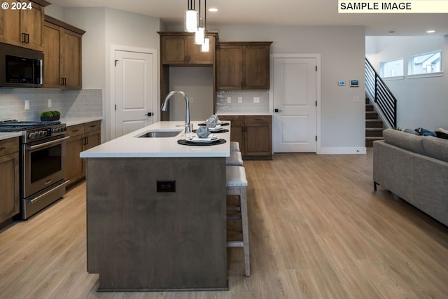 kitchen featuring stainless steel appliances, light hardwood / wood-style flooring, hanging light fixtures, and sink