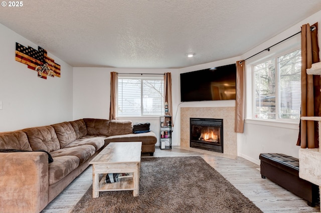 living room featuring a tile fireplace, a textured ceiling, and light hardwood / wood-style flooring