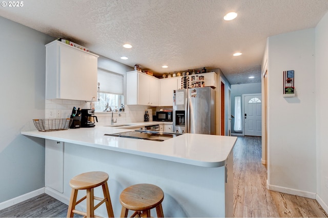 kitchen featuring kitchen peninsula, backsplash, black appliances, light hardwood / wood-style flooring, and white cabinets