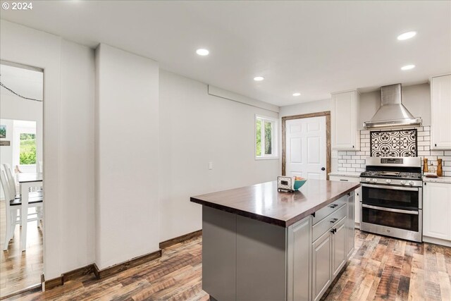 kitchen featuring range with two ovens, wall chimney range hood, hardwood / wood-style flooring, a kitchen island, and white cabinetry