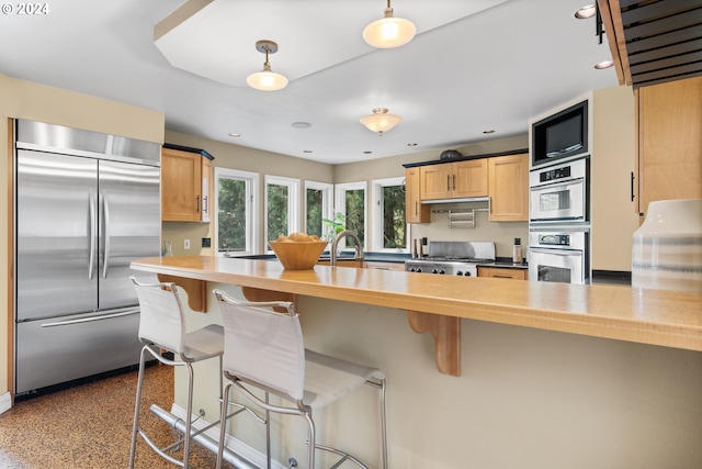 kitchen featuring light brown cabinets, stainless steel appliances, kitchen peninsula, and a breakfast bar area