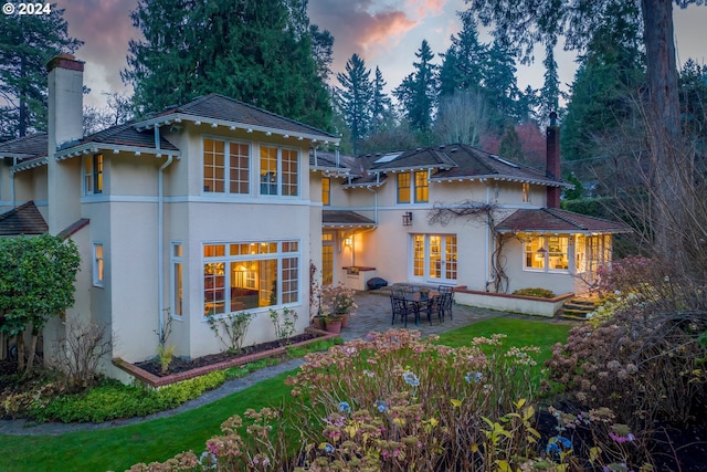 back house at dusk with a patio area and a yard