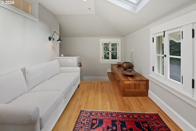 sitting room featuring lofted ceiling with skylight and light hardwood / wood-style flooring