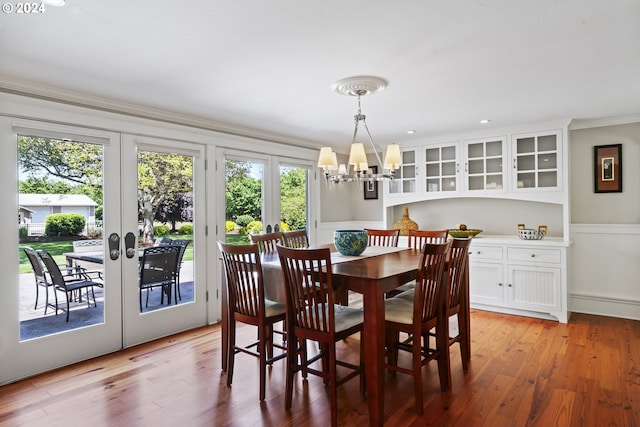 dining space with french doors, ornamental molding, a chandelier, and light wood-type flooring