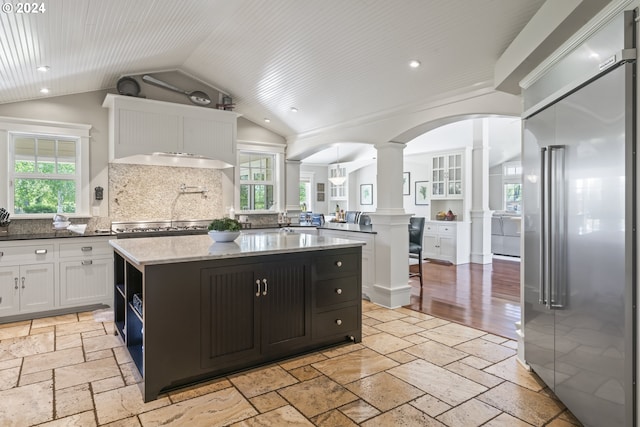 kitchen with a healthy amount of sunlight, lofted ceiling, a center island, and built in fridge