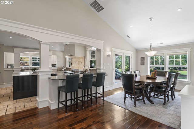 dining room featuring dark wood-type flooring, high vaulted ceiling, and decorative columns