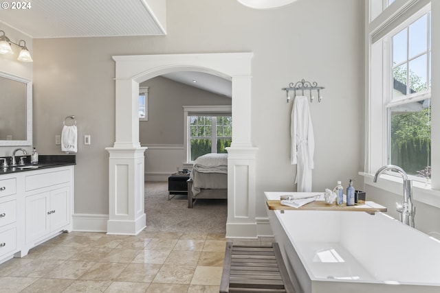 bathroom featuring vanity, a tub, ornate columns, and lofted ceiling