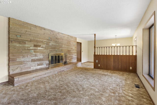 unfurnished living room featuring a stone fireplace, light colored carpet, a textured ceiling, and a notable chandelier