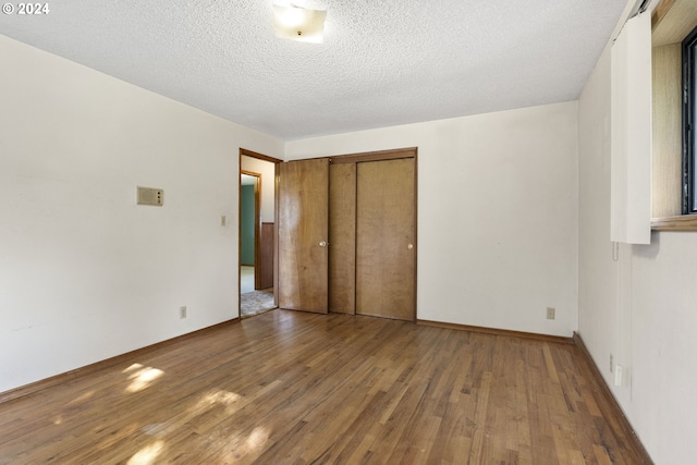 unfurnished bedroom with a closet, baseboards, wood finished floors, and a textured ceiling