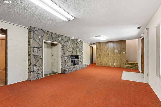 finished below grade area featuring a stone fireplace, carpet flooring, wooden walls, a textured ceiling, and visible vents