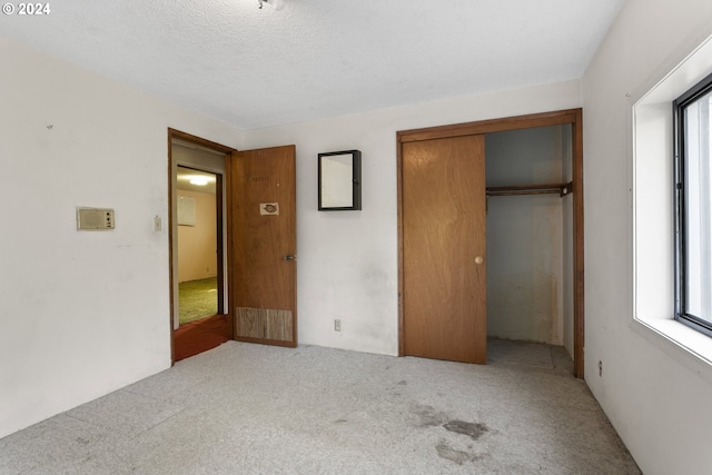 unfurnished bedroom with light colored carpet, a textured ceiling, a closet, and multiple windows