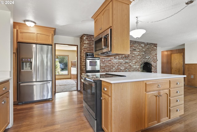 kitchen with appliances with stainless steel finishes, hardwood / wood-style flooring, pendant lighting, and a textured ceiling