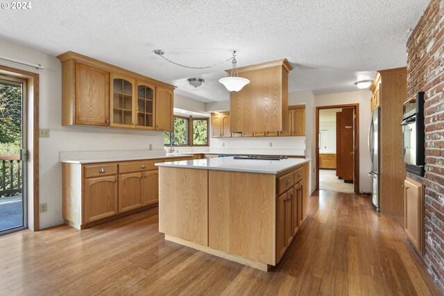 kitchen featuring glass insert cabinets, a center island, wood finished floors, light countertops, and oven