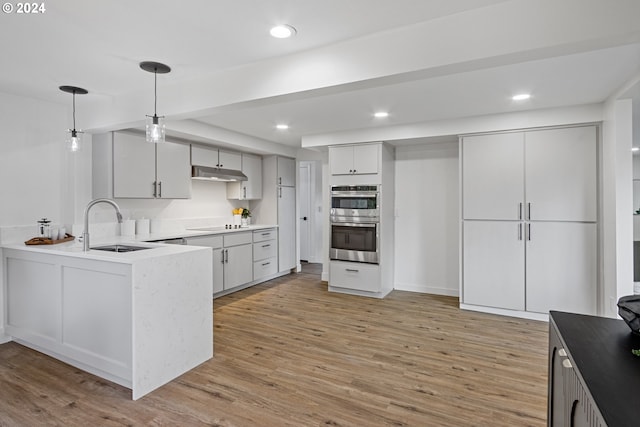 kitchen featuring sink, stainless steel double oven, light hardwood / wood-style flooring, kitchen peninsula, and pendant lighting