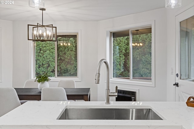 kitchen with light stone counters, sink, pendant lighting, and a notable chandelier