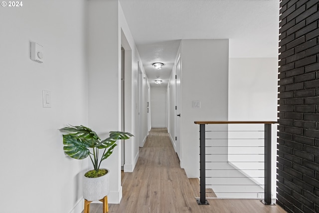 hall featuring a textured ceiling, light hardwood / wood-style floors, and brick wall