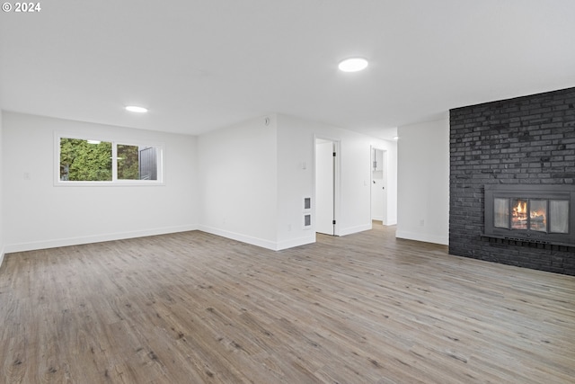 unfurnished living room with a brick fireplace and light wood-type flooring