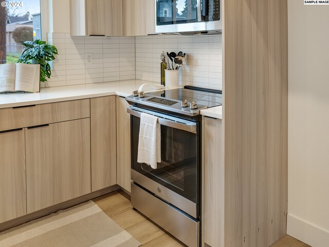 kitchen with light brown cabinetry, light wood-type flooring, stainless steel electric range, and tasteful backsplash