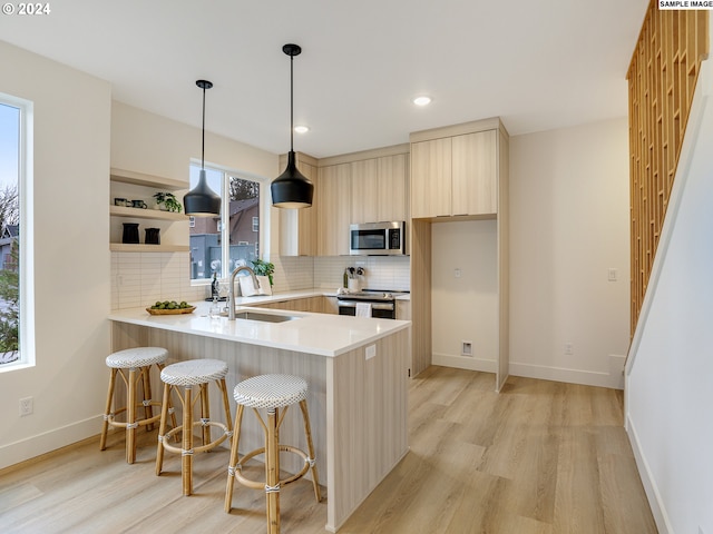 kitchen featuring appliances with stainless steel finishes, sink, kitchen peninsula, backsplash, and light wood-type flooring