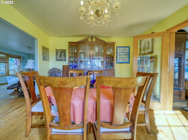 dining space featuring a textured ceiling, a notable chandelier, and light wood-type flooring