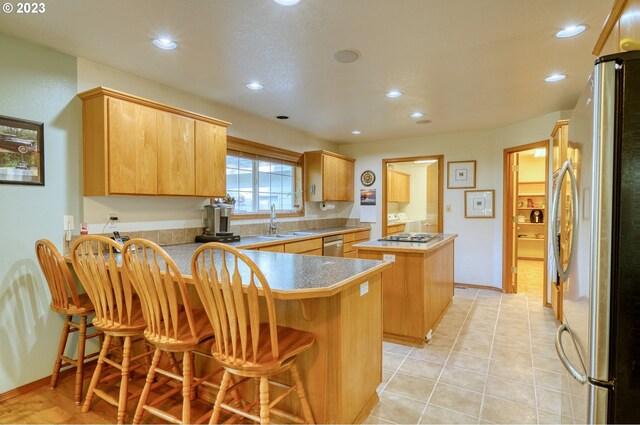 kitchen with kitchen peninsula, appliances with stainless steel finishes, sink, light tile floors, and a breakfast bar area