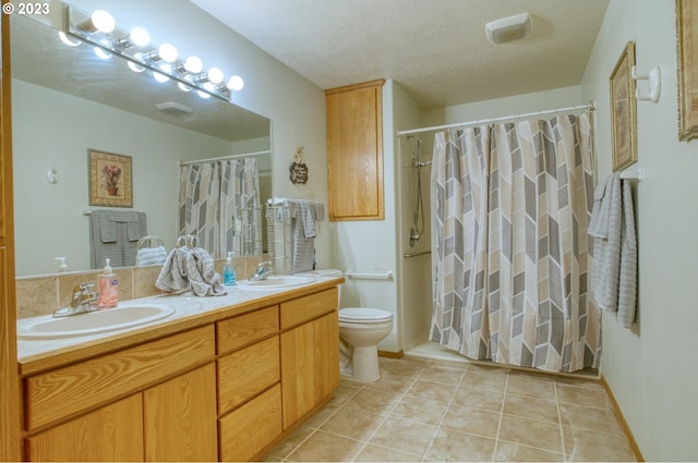 bathroom featuring toilet, vanity with extensive cabinet space, dual sinks, tile flooring, and a textured ceiling