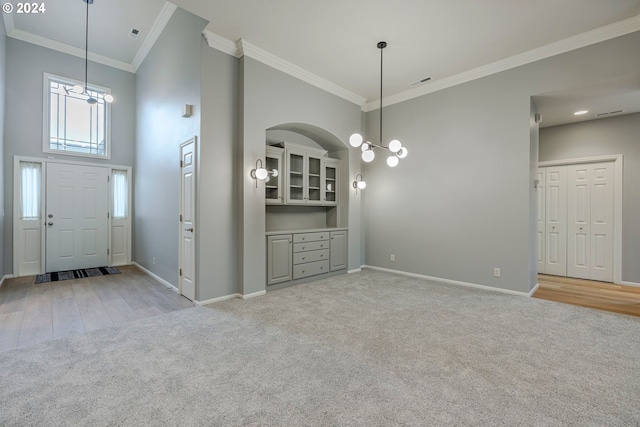 foyer featuring a chandelier, a towering ceiling, light hardwood / wood-style floors, and ornamental molding