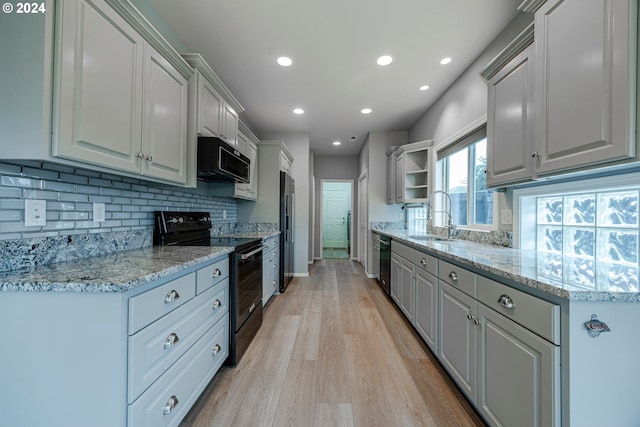 kitchen with sink, light wood-type flooring, light stone countertops, and black appliances