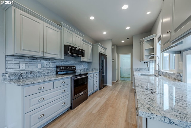 kitchen with light wood-type flooring, light stone counters, gray cabinetry, and black appliances