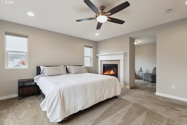 carpeted bedroom featuring a tiled fireplace and ceiling fan