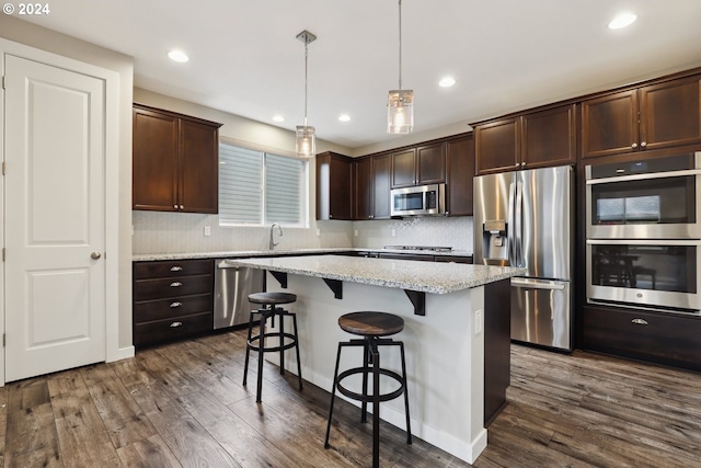 kitchen with pendant lighting, dark hardwood / wood-style flooring, a kitchen island, light stone counters, and stainless steel appliances