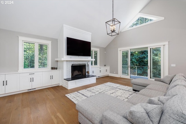 living room with light wood-type flooring, a fireplace, high vaulted ceiling, and a chandelier