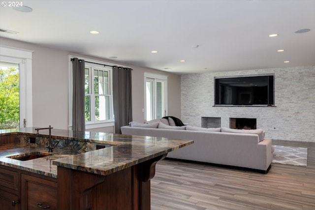 kitchen with a fireplace, light wood-type flooring, a breakfast bar, and dark stone countertops