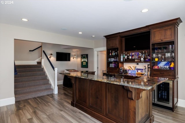 bar with wood-type flooring, dark brown cabinetry, and dark stone counters