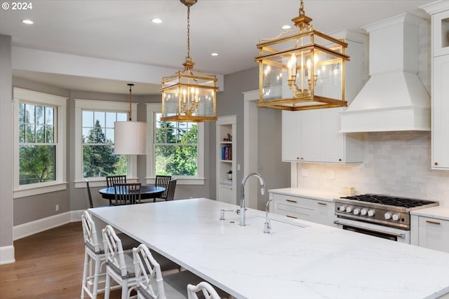 kitchen featuring premium range hood, hanging light fixtures, hardwood / wood-style flooring, high end stove, and white cabinetry