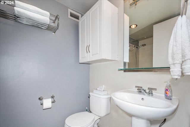 bathroom with tiled shower, sink, and toilet