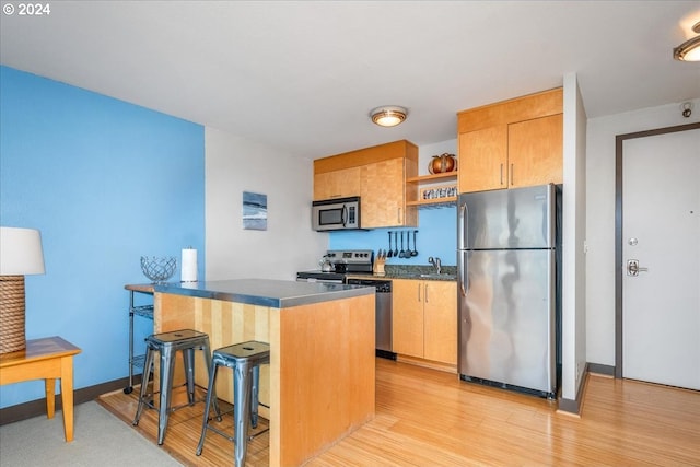 kitchen featuring appliances with stainless steel finishes, sink, a kitchen breakfast bar, and light hardwood / wood-style flooring