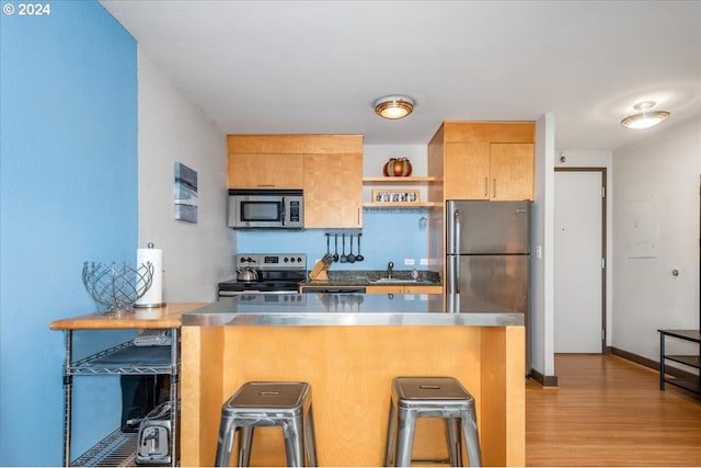 kitchen with stainless steel counters, light wood-type flooring, appliances with stainless steel finishes, a kitchen breakfast bar, and kitchen peninsula