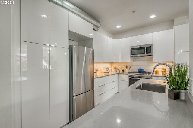 kitchen with stainless steel appliances, sink, tasteful backsplash, light stone countertops, and white cabinetry