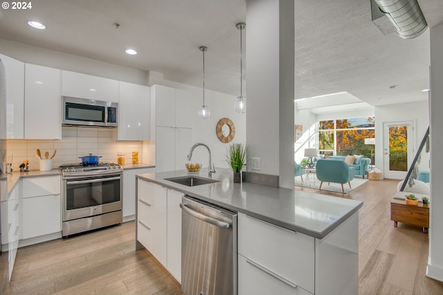 kitchen featuring decorative light fixtures, white cabinets, sink, and stainless steel appliances