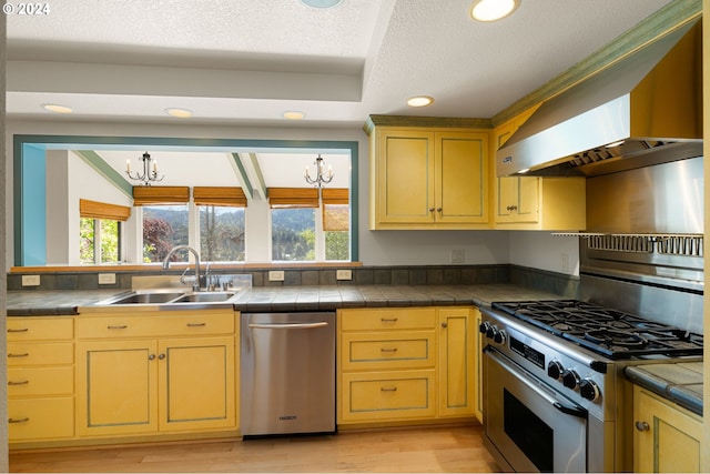 kitchen featuring wall chimney exhaust hood, a healthy amount of sunlight, appliances with stainless steel finishes, and sink