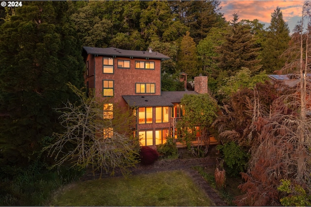 back house at dusk with a wooden deck and a yard