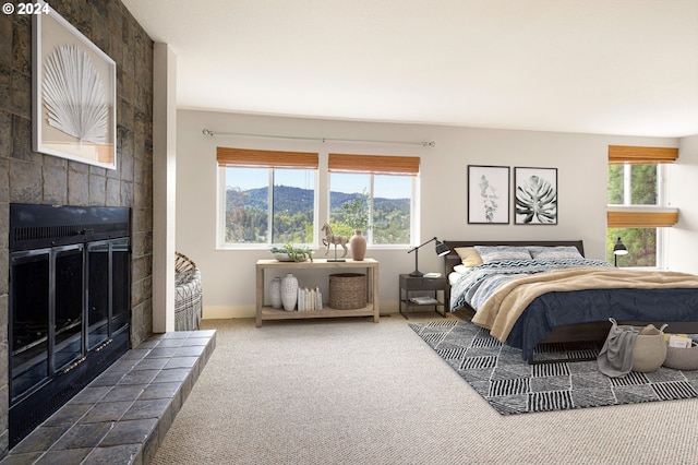 bedroom featuring a tiled fireplace, a mountain view, carpet floors, and multiple windows