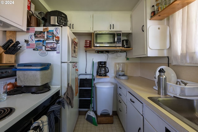 kitchen with crown molding, light tile flooring, range, sink, and white cabinetry