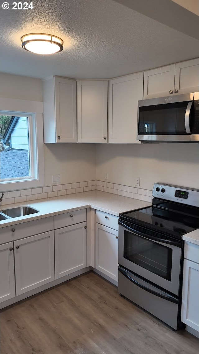 kitchen featuring appliances with stainless steel finishes, a textured ceiling, light hardwood / wood-style floors, and white cabinetry