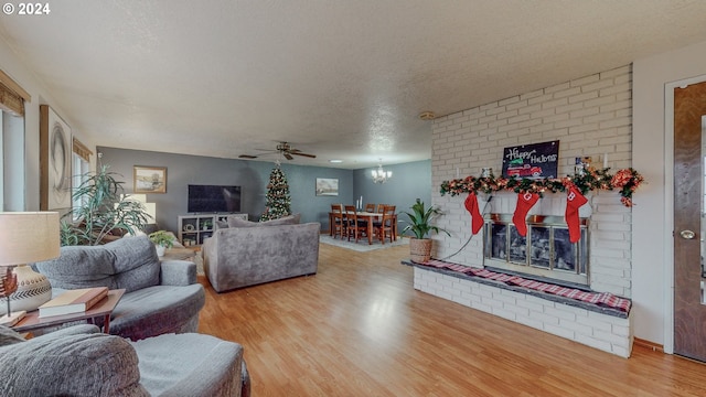 living room with hardwood / wood-style floors, ceiling fan with notable chandelier, a fireplace, and a textured ceiling