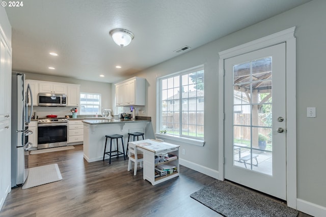 kitchen with kitchen peninsula, white cabinets, a kitchen bar, appliances with stainless steel finishes, and dark hardwood / wood-style flooring