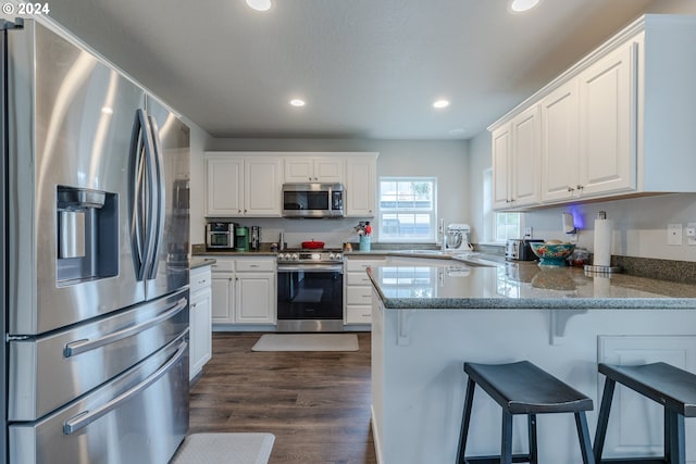 kitchen with kitchen peninsula, a kitchen breakfast bar, white cabinetry, dark wood-type flooring, and stainless steel appliances