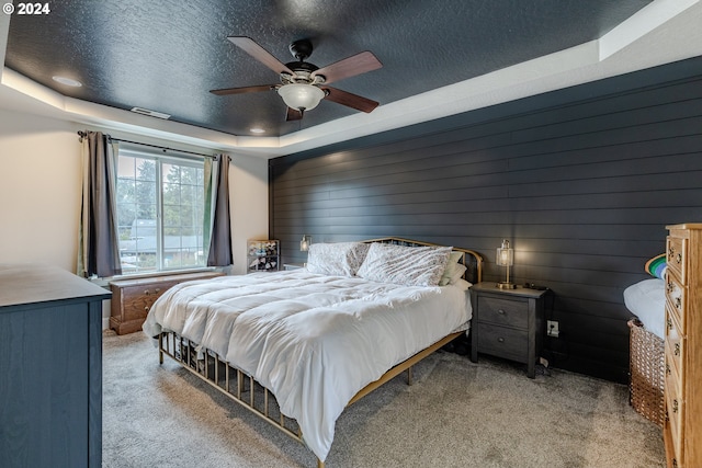 bedroom with ceiling fan, light carpet, a textured ceiling, and a tray ceiling