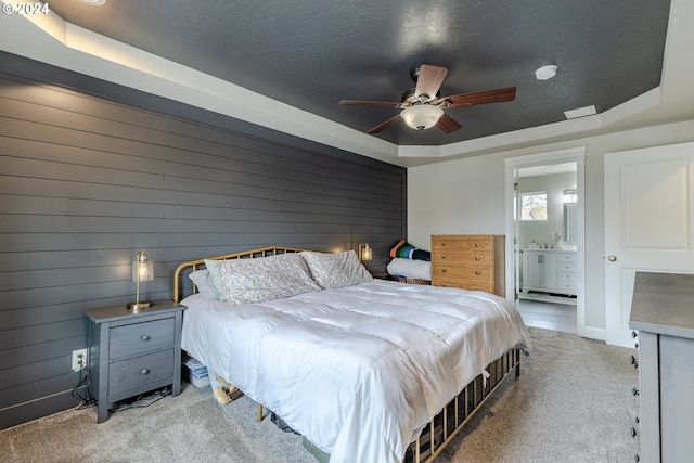 bedroom featuring ensuite bath, a raised ceiling, ceiling fan, light carpet, and wooden walls